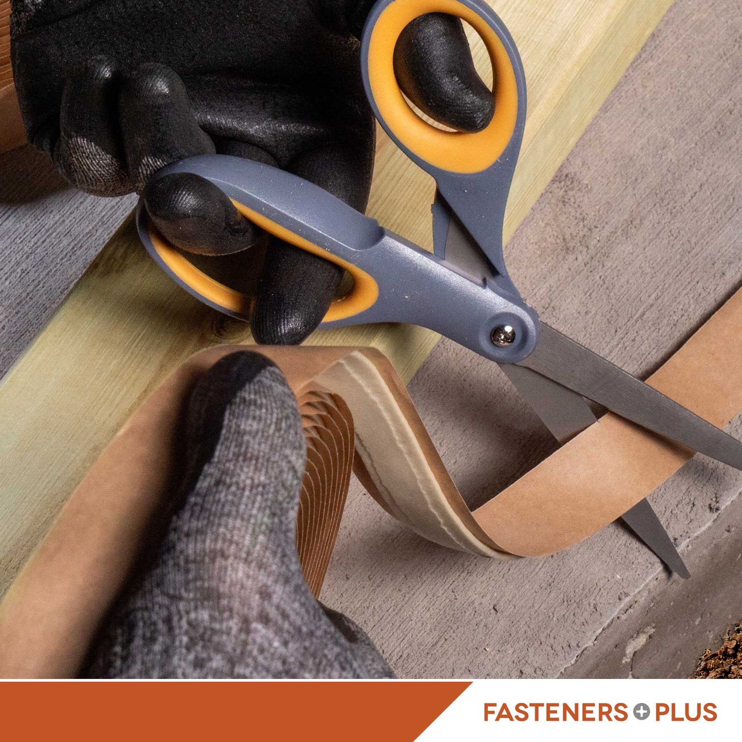 Person cutting a strip of butyl tape with a pair of scissors on a concrete surface, wearing gloves.