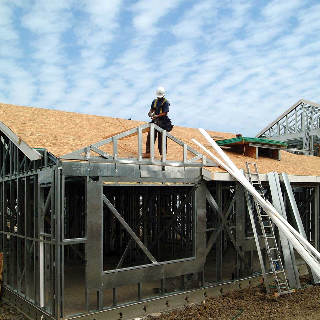 Construction site with a partially built house and a worker on the roof.