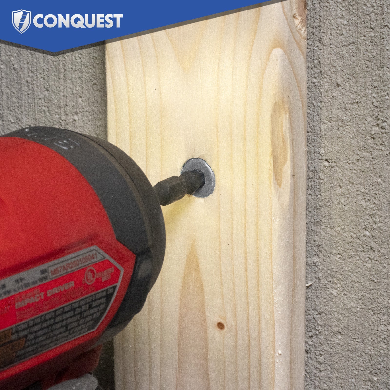 Red drill being used on a wooden block with concrete wall background, featuring the Conquest brand.
