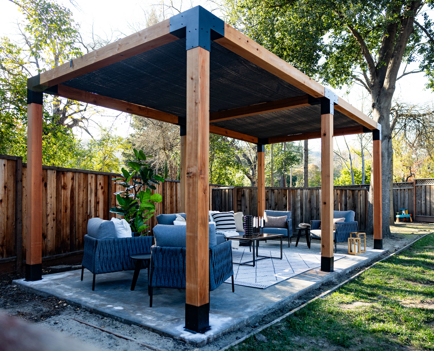 Outdoor patio with wooden pergola, chairs, and table in a backyard setting.