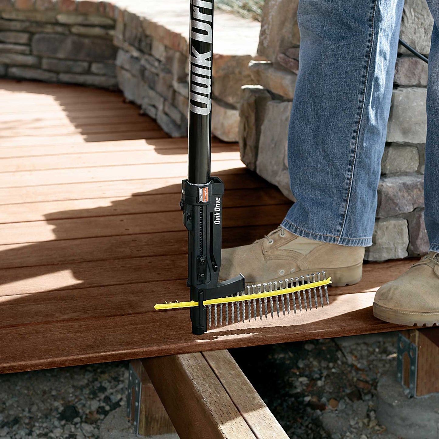 Person using a Quik Drive tool on a wooden surface with a stone wall background