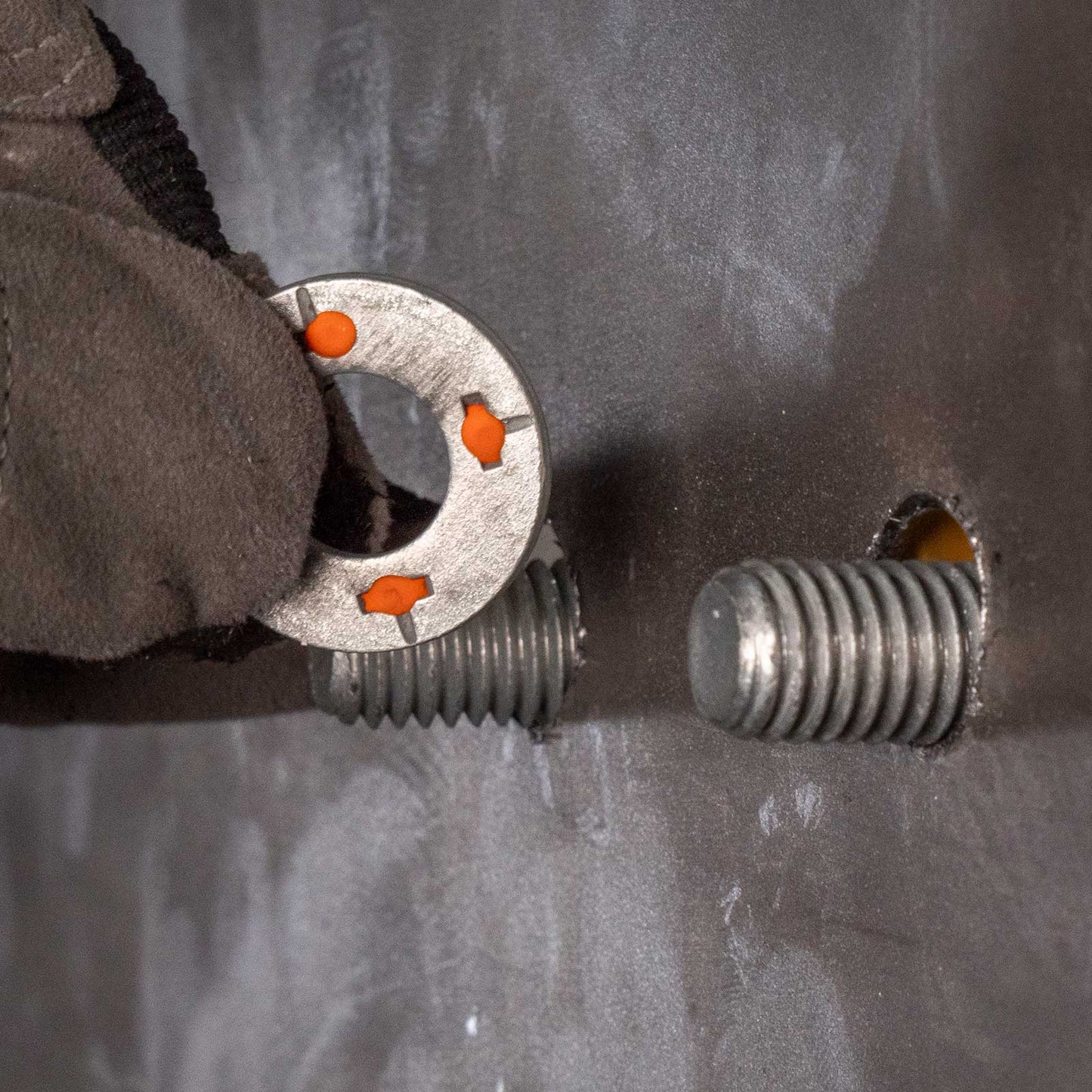 a gloved hand putting a squirter washer on a threaded bolts