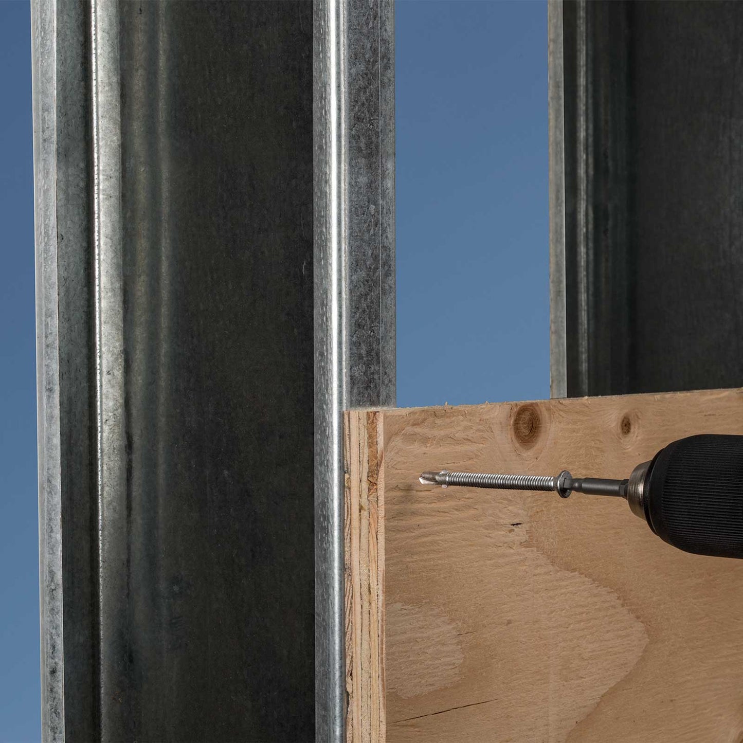 Wooden board with a screw and drill bit against a metal frame and blue sky background