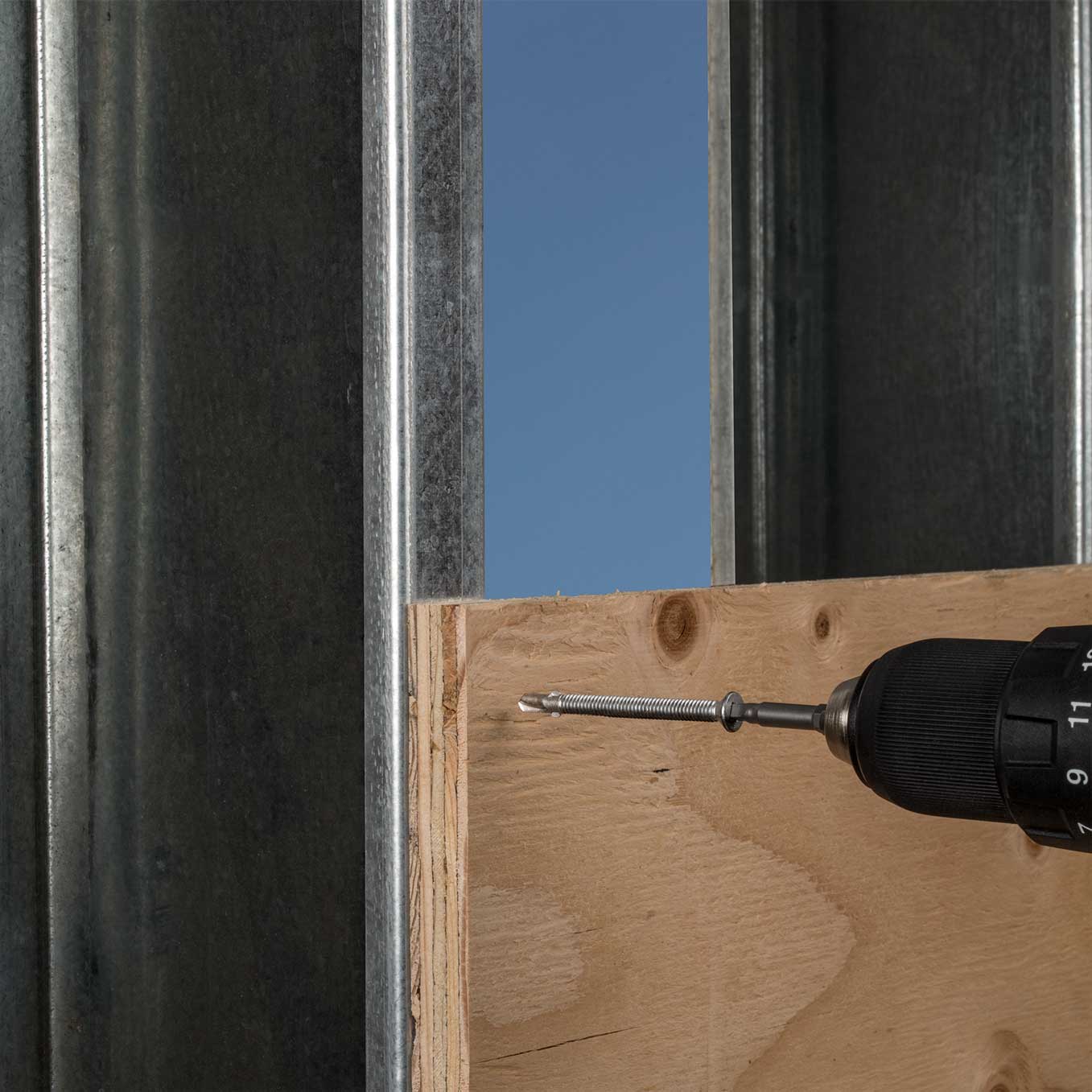 Drill bit being inserted into a wooden surface with a clear blue sky in the background