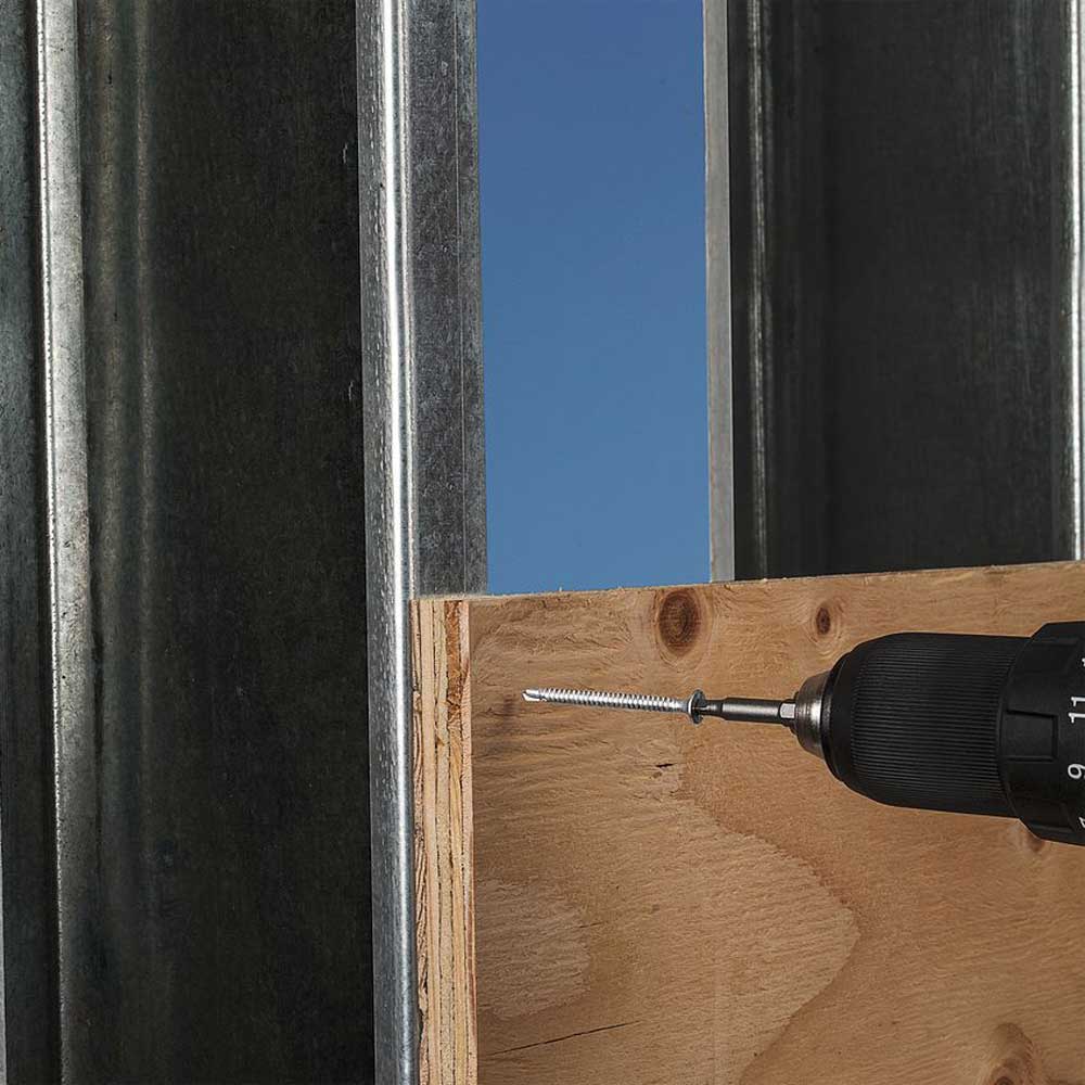 Drill with a screw on a wooden surface against a blue sky background