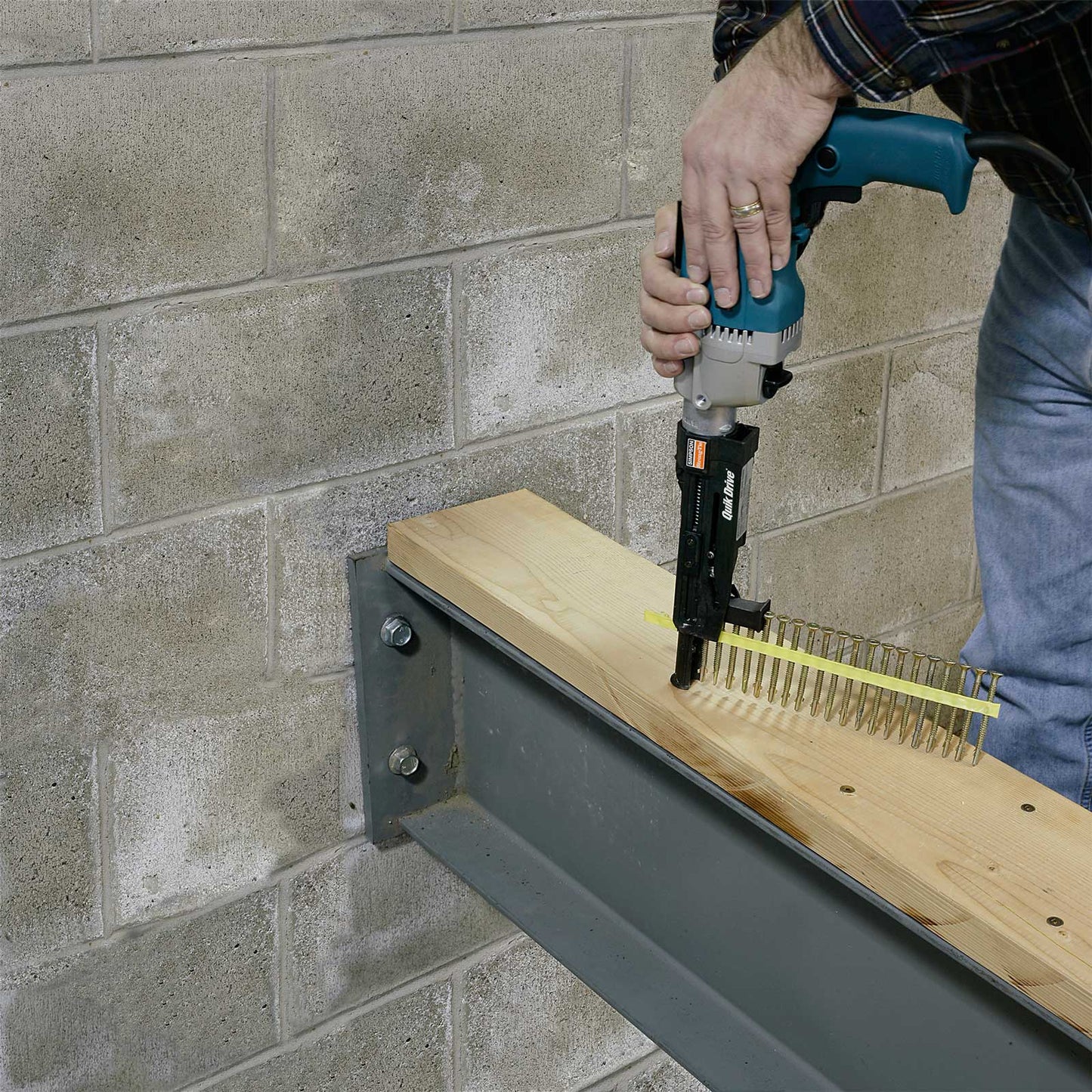 Person using a nail gun on a wooden shelf against a brick wall.