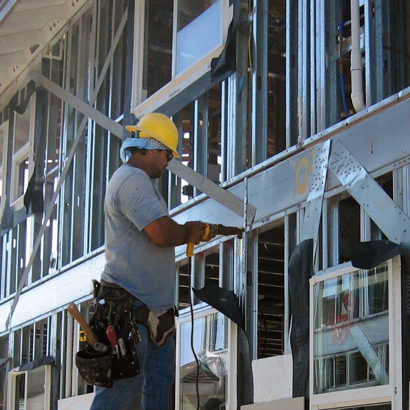 Worker on a construction site wearing a yellow helmet and tool belt.