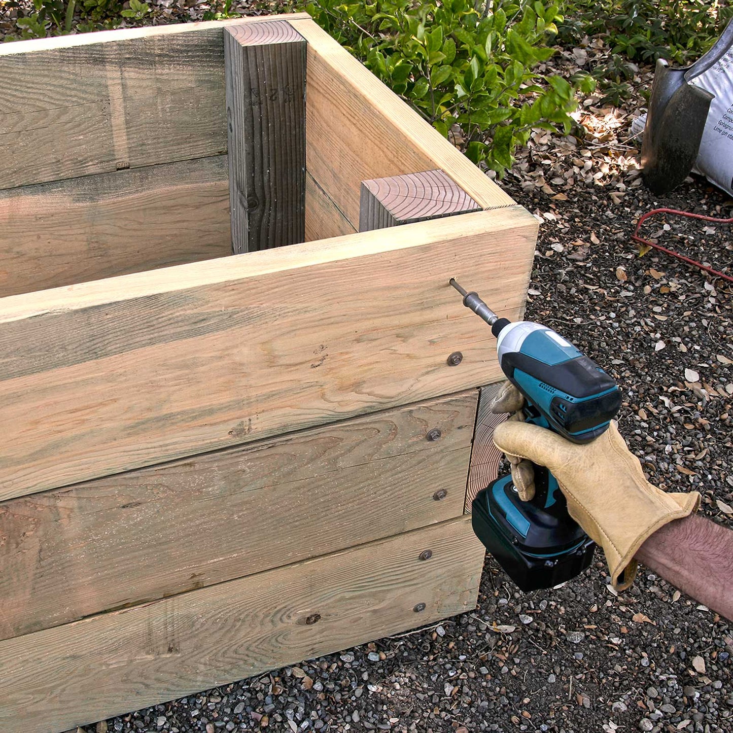 Wooden raised garden bed planter box with a power drill installing timber screws