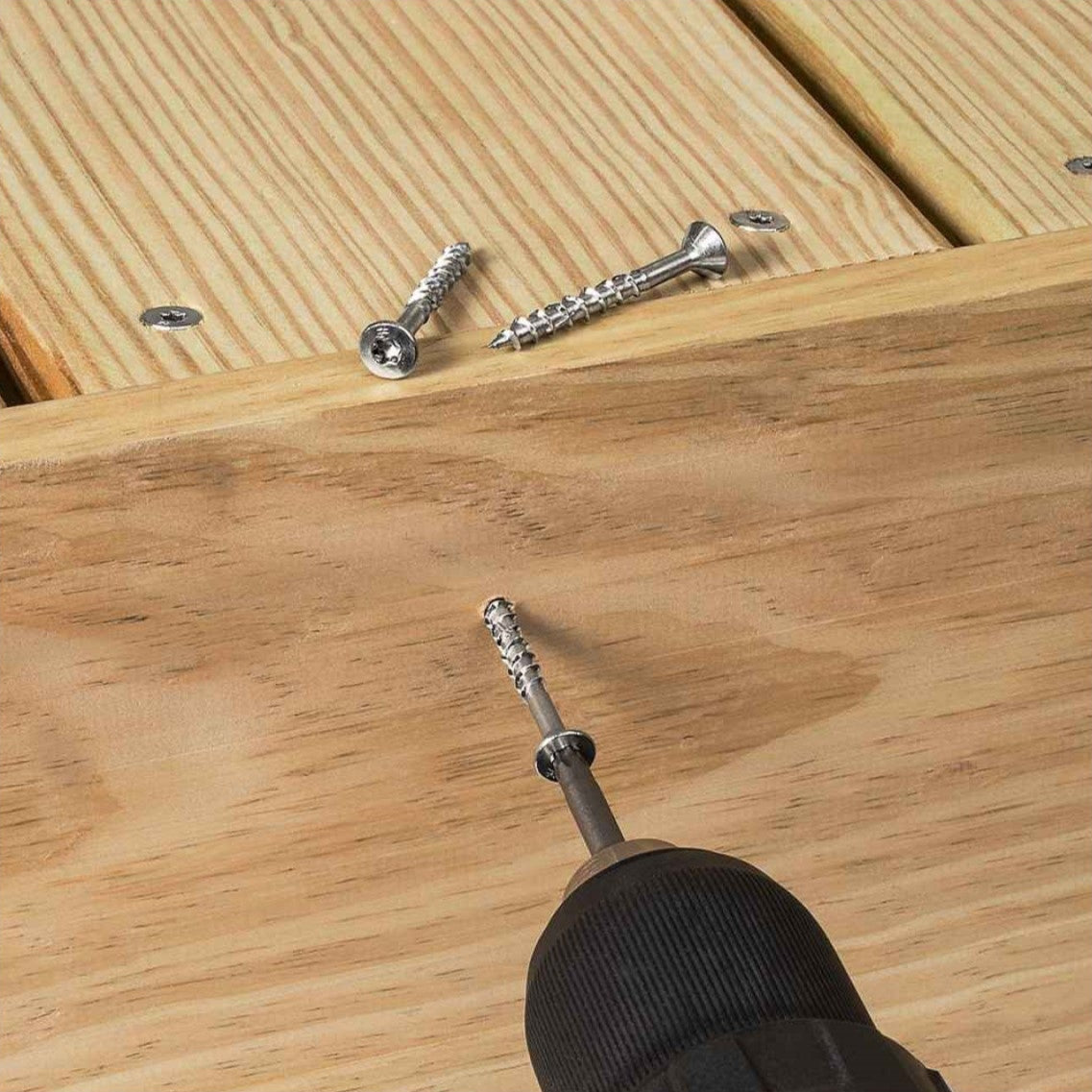 Screws on a wooden surface with a drill drilling a screw
