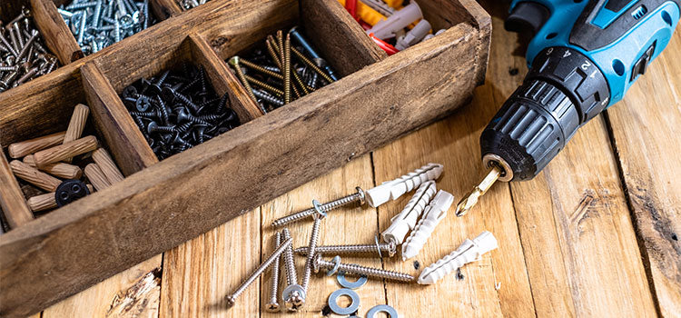 Blue and black drill laying on a table near a wooden box containing screws, washers, and plastic anchors.