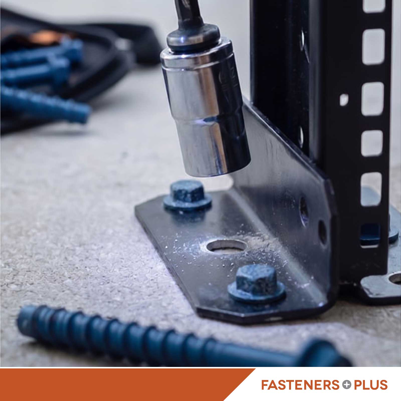 Close-up of a black metal mounting bracket being secured with a socket wrench and blue concrete anchor screws