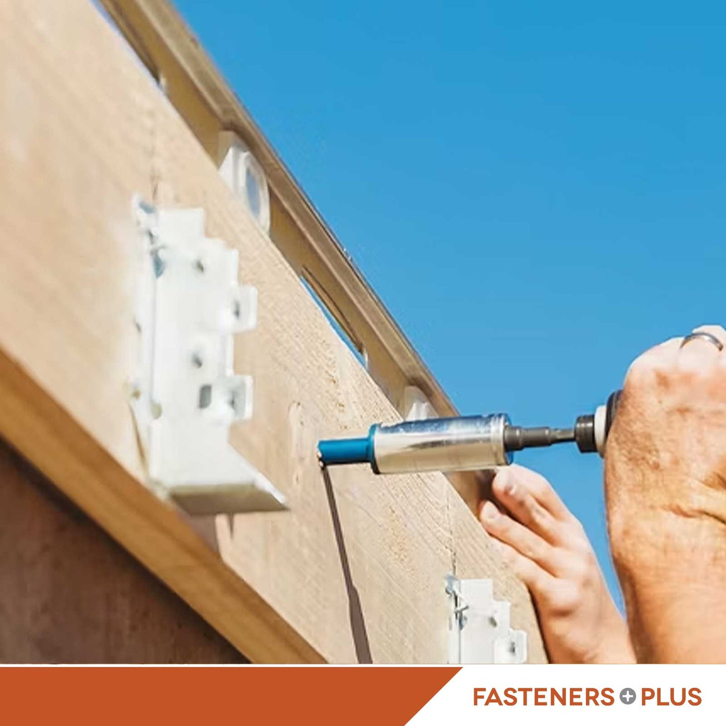 A person using a drill to install blue concrete screw anchors into wood on a concrete wall