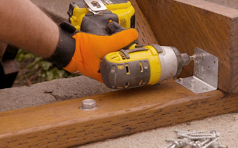 Person using a power drill on wooden planks and metal framing angles with a blurred background