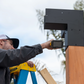 Person on a ladder showing how to drill Simpson Sage Corner Connector to a Wood Post
