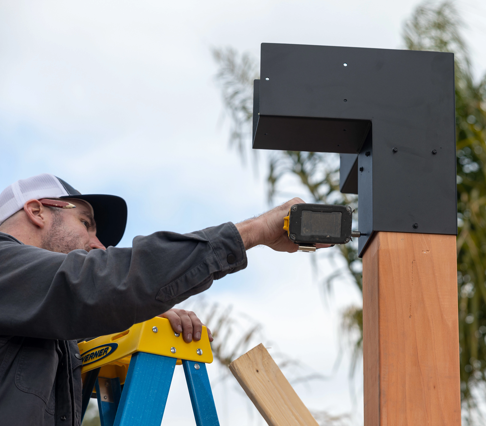 Person on a ladder showing how to drill Simpson Sage Corner Connector to a Wood Post