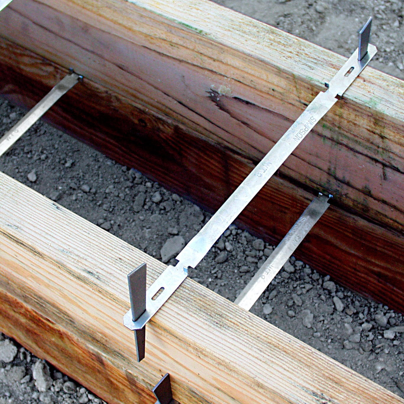 Wooden beams with metal brackets on a gravel surface