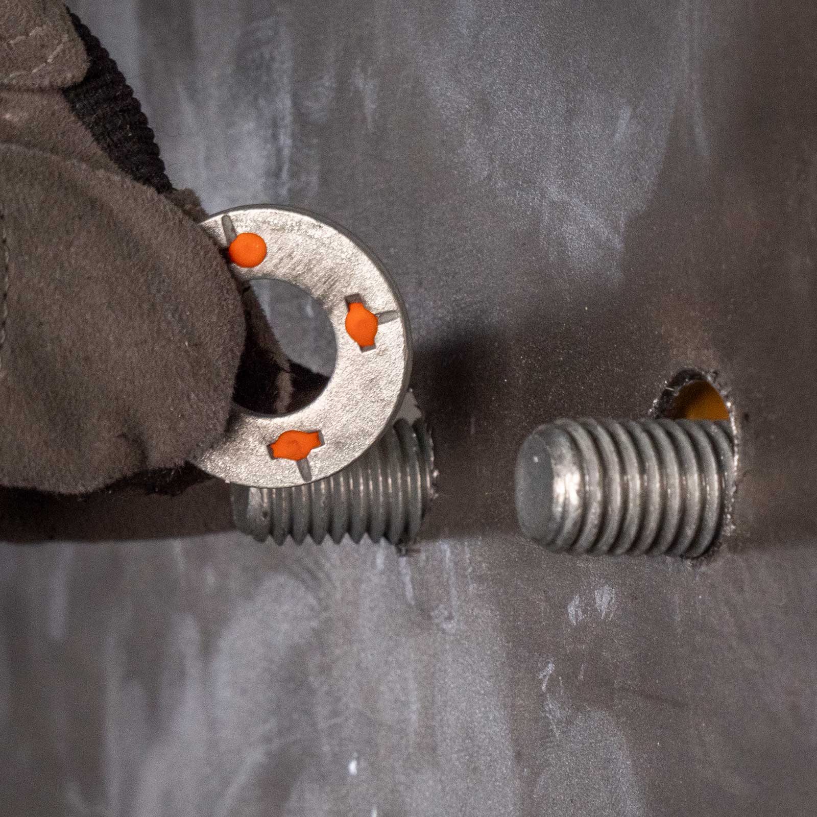 a gloved hand putting a squirter washer on a threaded bolts