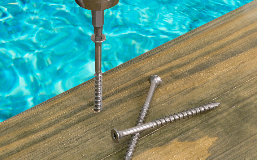 Drill bit and screws on a wooden surface with a pool in the background