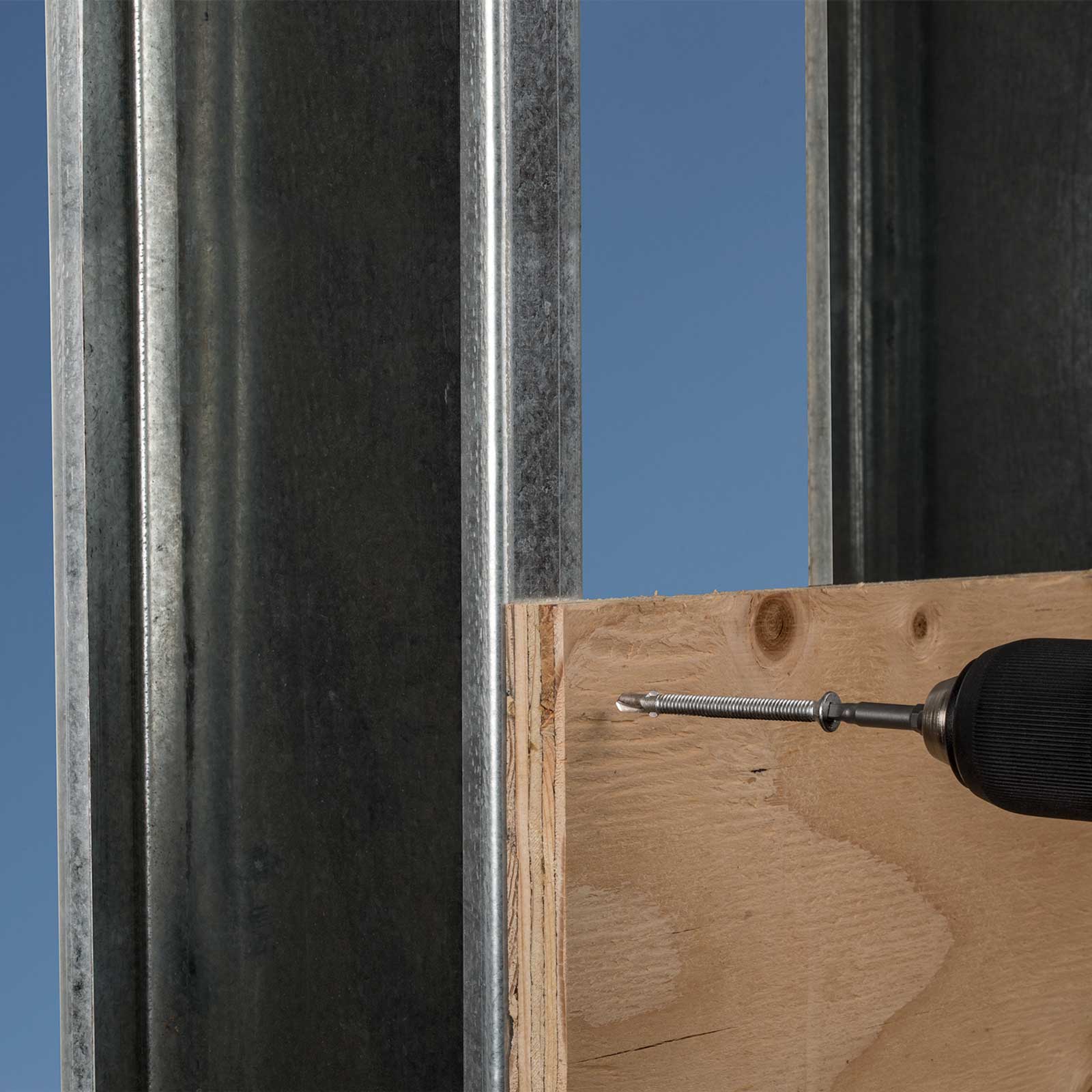 Wooden board with a screw and drill bit against a metal frame and blue sky background