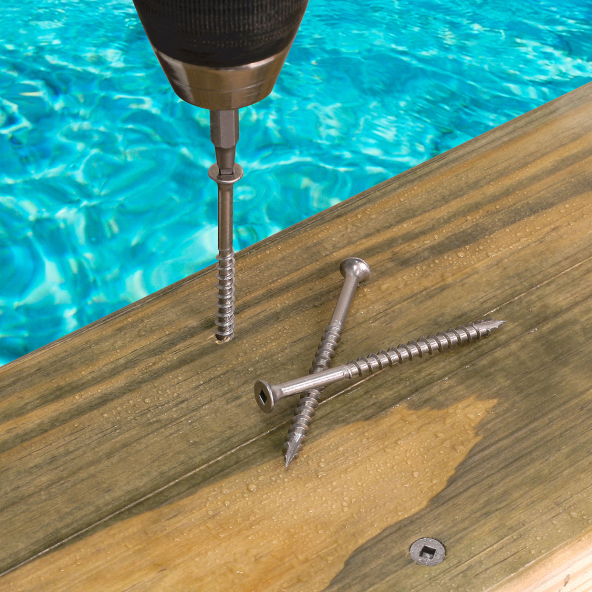 Drill driving screws into a wooden surface with a pool in the background