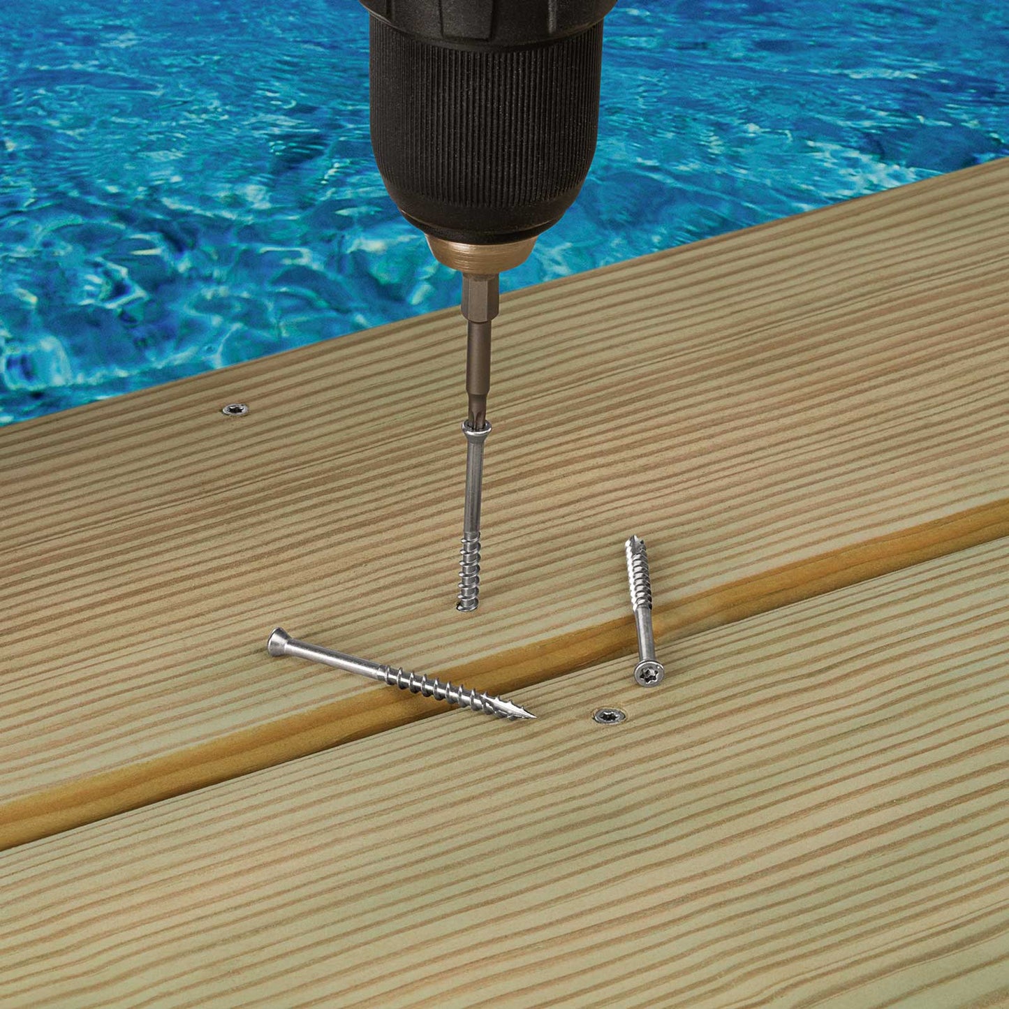Drill bit being used to drive screws into wooden planks with a pool in the background