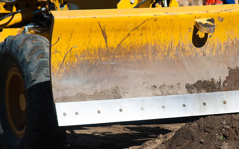 Close-up of a yellow bulldozer blade with dirt and wear on a construction site.