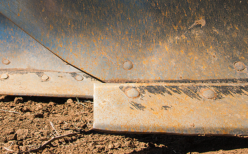 Rust-covered metal plow on a dirt ground with plow bolts