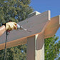 Person using a drill and timber screws on wooden beams with trees and blue sky in the background