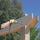 Person using a drill on a wooden structure with trees and blue sky in the background