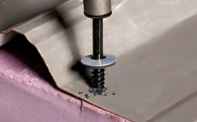 Screw penetrating a piece of metal on top of concrete with a close-up view.