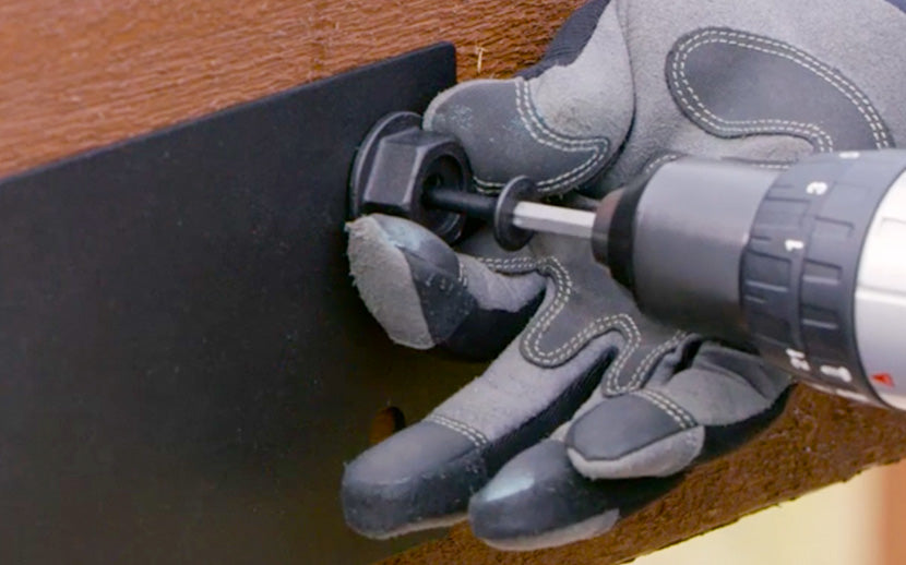 Person using a drill on a piece of wood with protective gloves.