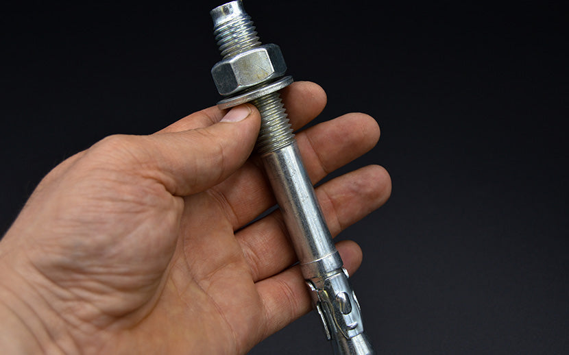 Hand holding a wedge anchor against a black background